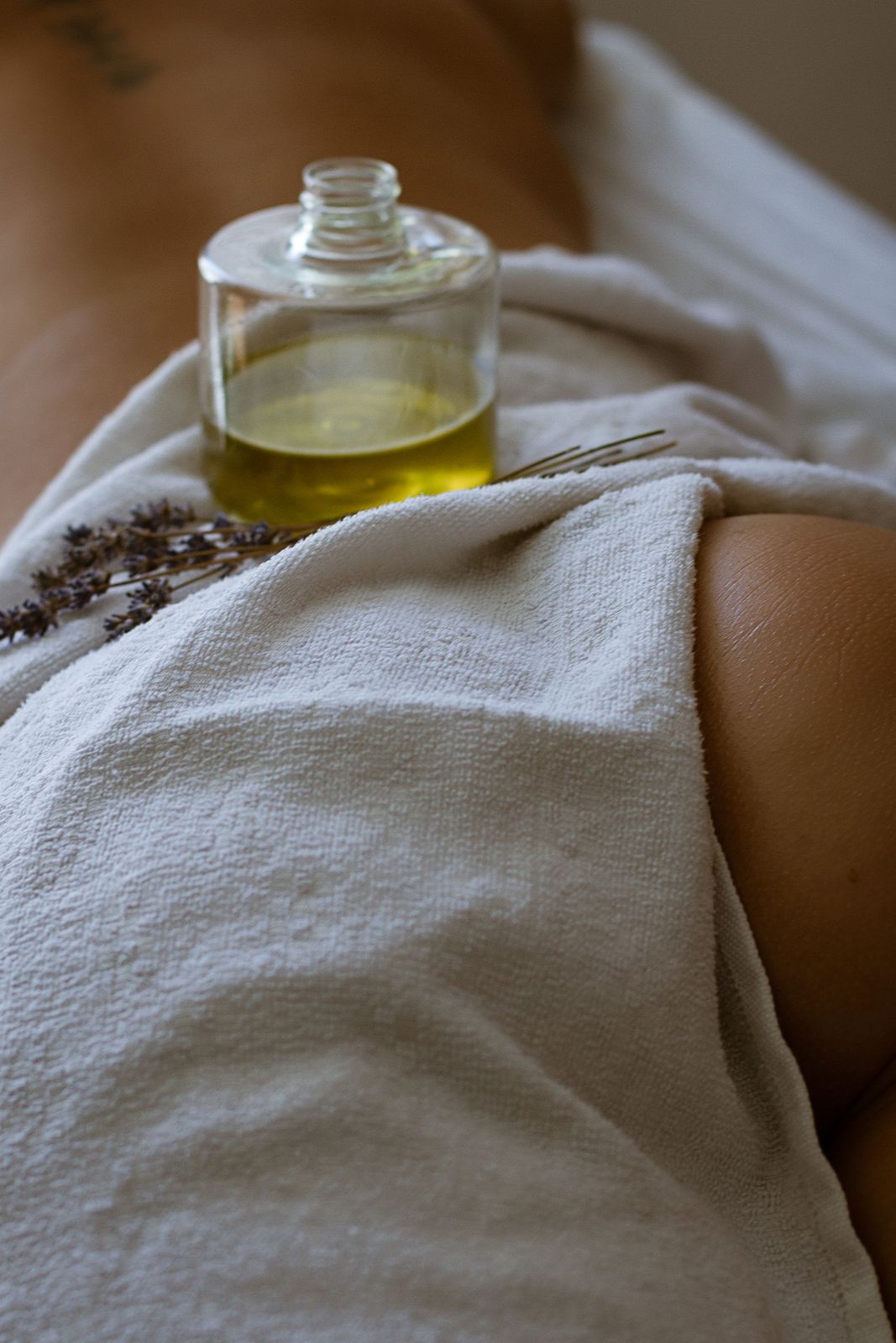 Massage oil and dried lavender resting on draped linen