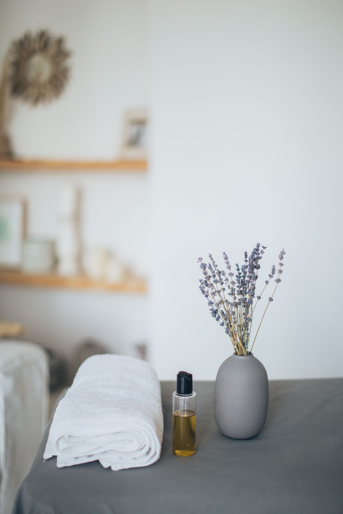 Folded towel, massage oil and a single stem on a treatment side table