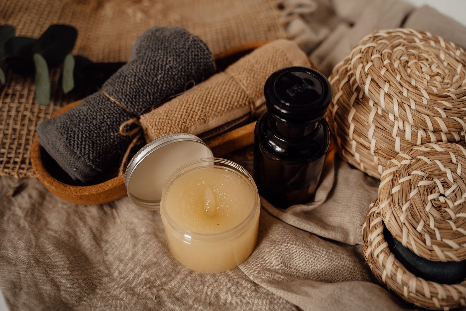Rolled spa towels, balm, and massage oils in a warm flat lay